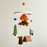 A colorful wool felt camping baby mobile is displayed against a pale neutral background. It features multiple handcrafted felt elements suspended from a white felt ring. Figures include a campfire, green pine tree, blue and white bear-adorned kayak, brown camping tent, backpack, and blue minivan, with blue and pink felt balls. Each element is made from textured wool felt with vivid colors and careful detailing, bringing the camping theme to life.
