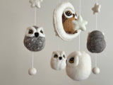A wool felt baby mobile featuring an owl theme, suspended from a wooden frame with multiple owls of varying sizes and colors. Each owl has distinct features such as large eyes, small wings, and a round body, creating a playful and whimsical atmosphere in the child's room.