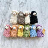 Ten handcrafted wool felt Candy Sheep finger puppets are displayed in two rows on a mottled white and gray surface. These charming, soft, and fluffy sheep finger puppets feature sweet smiles and small ears. Four felt sheep come in white, brown, cream, and black, while six others are vibrant pink, orange, yellow, green, blue, and purple, perfect for imaginative play.