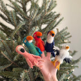 A wool felt eagle finger puppet is playfully displayed against a blurred Christmas tree backdrop. This handcrafted felted finger puppet showcases the eagle's distinctive, lifelike appearance and textured details, reflecting its artisanal quality.