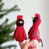 A needle-felted blue jay finger puppet is playfully displayed on a hand, set against a blurred Christmas tree background, evoking holiday cheer. This unique handcrafted blue jay puppet showcases striking blue feathers on its head, wings, and tail, complete with a distinctive crest. It highlights the charm of fair-trade, handmade creations by skilled Nepali artisans.