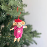 A charming needle felted Christmas mouse ornament from the set dangles from a lush green Christmas tree. This handcrafted 3D wool felt mouse wears a red hat and a pink dress with a white flower. A red cotton string is attached to its hat, allowing it to hang gracefully among the branches.