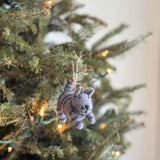 A charming gray tabby cat felt Christmas ornament hangs on a brightly lit Christmas tree branch. This handmade felt cat ornament features intricate black stripes on its gray body, with a delicate stitched black nose and whiskers, evoking a joyful holiday mood.