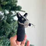 A handmade wool felt turtle finger puppet is held by a female hand against a soft white backdrop and green Christmas tree needles. This charming, needle-felted 3D felt turtle puppet, crafted from 100% wool, showcases its tactile texture and handcrafted quality, making it an ideal kids' toy for imaginative finger play.