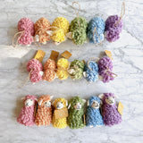 A cheerful set of six mini felt fluffy sheep ornaments is arranged in rows on a white marble surface. These soft, felted wool sheep ornaments feature fluffy textures in a variety of pastel tones, including pink, beige, yellow, green, blue, and purple. Each ornament includes a jute string for easy hanging.
