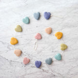 A cheerful felt star garland is artfully arranged in a circular shape on a marbled surface. It features seven pastel rainbow-hued felt stars in shades of blue, purple, pink, yellow, and green. The stars are evenly spaced along a white cotton string, creating a symmetrical and decorative design.