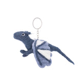 A handmade felt flying dragon keychain is presented against a stark white background. This unique wool felt keychain features a detailed dragon in blended gray and blue hues with contrasting white wings and a slender tail. A metal clasp is attached, completing the design.