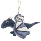 A needle-felted flying dragon ornament is suspended by a jute string against a stark white background. This whimsical wool felt dragon features a blue body with contrasting white wings and horn tips, and small beady eyes.