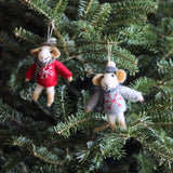 A charming felt mouse ornament, dressed in winter attire, hangs from a vibrant green Christmas tree branch. This handcrafted wool felt mouse features a light beige face, rounded ears, and a small tail. It wears a red sweater with a white snowflake design and a gray scarf, adding a festive and joyful touch to the tree.