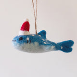 A smiley whale shark felt ornament is suspended by a jute string against a plain white background. This handcrafted felt whale shark ornament features a charming gradient, transitioning from light gray on its lower half to vibrant blue on its upper body, adorned with white spots and a friendly smile.