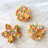 Three sets of handcrafted felt coasters rest on a marbled surface. Each coaster is made from half-inch wool felt balls in soft pastel colors including white, green, pink, orange, and light blue. The coasters come in three distinct shapes—round, star, and heart—and are tied together with jute twine and a small branded tag. Ethically handmade by Nepalese female artisans using 100% organic lamb wool, these coasters bring a soft, playful charm to any home decor.