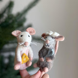 A white needle felted mouse finger puppet holding a yellow cheese is held by a female hand against a soft background. This handcrafted wool felt finger puppet features charming pink accents on its ears and feet, along with small black eyes. Made from high-quality, eco-friendly organic wool, this unique felt toy is a testament to skilled craftsmanship.