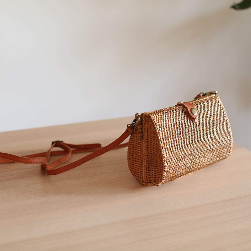 Bali Envelope Rattan Crossbody Bag handmade by Ganapati Crafts Co. in Bali sitting on a wood table with sun coming from the window creating a sense of luxury holidays