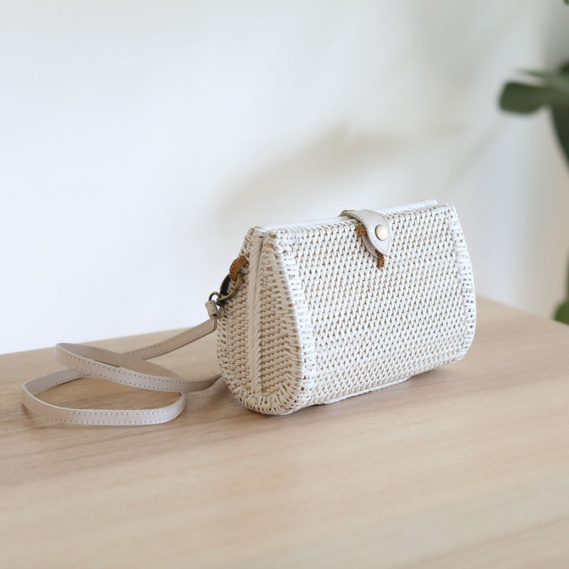 Bali Envelope Rattan Crossbody Bag handmade by Ganapati Crafts Co. in Bali sitting on a wood table with sun coming from the window creating a sense of luxury holidays