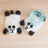 Two handcrafted wool felt panda coasters are displayed on a light wooden surface. One felt panda coaster lies flat, while the other supports a clear glass of water. These unique coasters feature a cheerful panda bear design, primarily white with black accents for ears, arms, and facial details. The visible wool felt texture highlights their soft, ethically handmade craftsmanship, supporting female artisans.