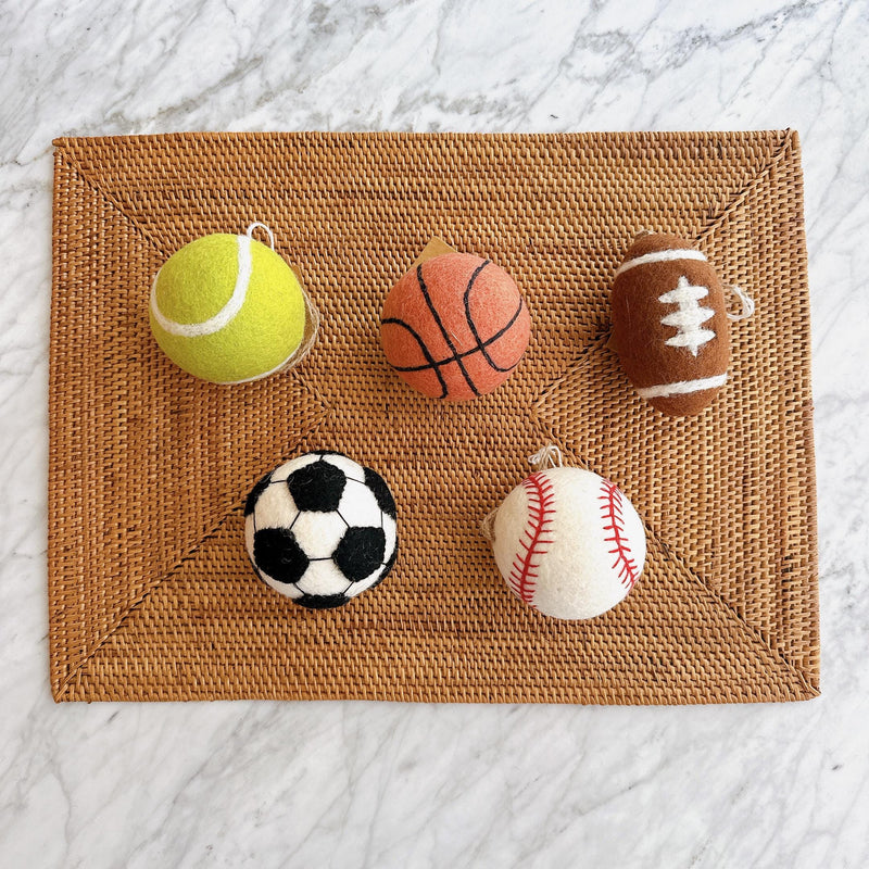 A set of five wool felt American popular sports ball ornaments rests on a woven mat against a marble background. These 3-inch, 3D needle felted ornaments include a yellow tennis ball, orange basketball, brown football with white accents, classic black and white soccer ball, and white baseball with red stitching. Each handcrafted sports ornament has a jute thread for easy hanging.