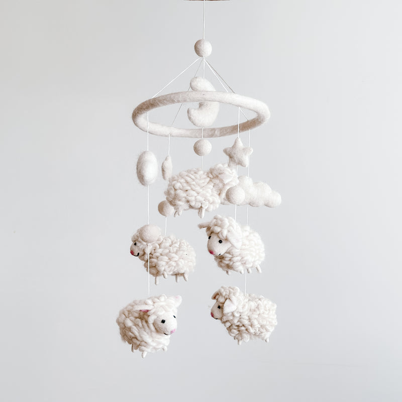 A handmade mobile featuring soft, organic wool felt sheep suspended from a central felt hoop, against a minimalist white background. The mobile's gentle movement creates a peaceful atmosphere, perfect for a baby's nursery.