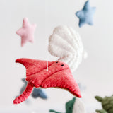 A mobile featuring sea creatures like scallops, sea turtles, sea horses, whales, dolphins, and stingrays hangs from the ceiling. The colorful mobile is made of wool felt, wood, and plastic, with a white background that contrasts beautifully with its vibrant colors.