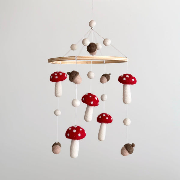 A handcrafted wool felt baby mobile, featuring a natural wooden hoop and suspended felt mushrooms and acorns in earthy tones. The mobile is designed for decorative use only, adding a touch of woodland magic to any nursery.