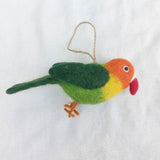 A vibrant handmade 100% wool felt parrot ornament is presented flat against a clean white background. This cheerful felt bird ornament features a color gradient, transitioning from orange on its head to yellow and green on its body. It has small orange felt legs, a red beak, and a jute string for hanging.