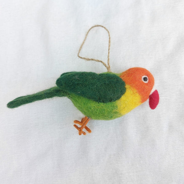 A vibrant handmade 100% wool felt parrot ornament is presented flat against a clean white background. This cheerful felt bird ornament features a color gradient, transitioning from orange on its head to yellow and green on its body. It has small orange felt legs, a red beak, and a jute string for hanging.