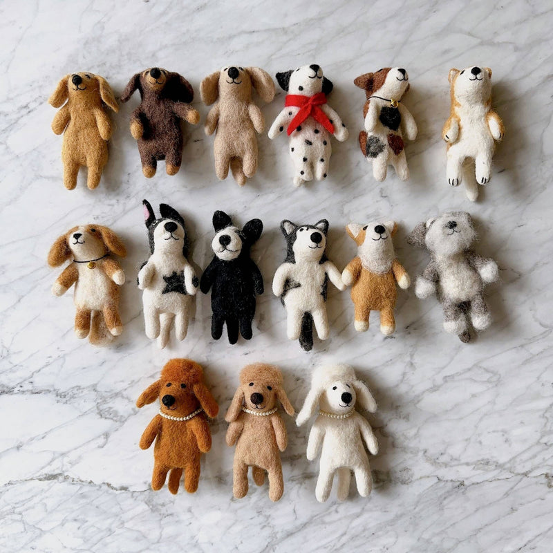 A felt Cavalier King Charles Spaniel finger puppet is displayed on a light marble backdrop. This wool felt finger puppet features fluffy ears, a captivating smile, an adorable love spot, and a bell necklace, all crafted with meticulous needle felt details.