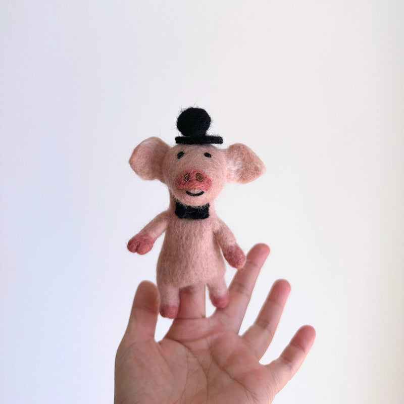A felt duck finger puppet, a type of handcrafted felt finger puppet, is gently supported upright in a female hand against a plain white backdrop. This unique needle felted duck wears a formal black top hat and a matching bow tie, highlighting its charming design.