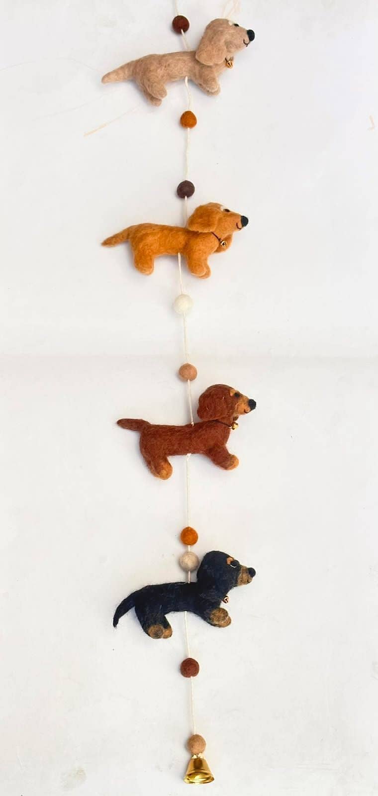 A colorful felt garland featuring four Dachshund puppies, displayed on a white background within a white felt frame. The garland is crafted with cream, khaki, brown, and black felt puppies in various colors, arranged in a line with a felt bone at the center. Made from wool felt, this playful and whimsical garland is perfect for decorating a child's room or as a thematic accessory.