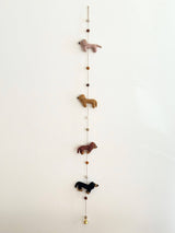 A colorful felt garland featuring four adorable dachshunds in cream, khaki, brown, and black, arranged in a line with the largest at the center. A felt bone is also present on the garland, set against a plain white background.