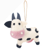 A handmade wool felt milk cow ornament is displayed against a plain white backdrop. This whimsical felt milk cow features a cream-colored body with black spots, blue horns, and a pink face. A jute string is attached for easy hanging.