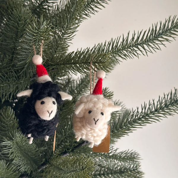 Two sheep ornaments with Santa hats hanging on a Christmas tree branch.