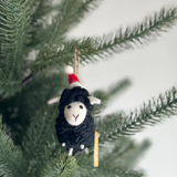 Decorative sheep ornament with a Santa hat hanging on a Christmas tree branch.