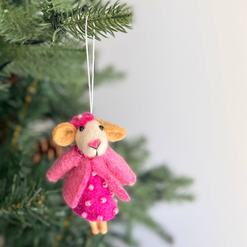 A handcrafted needle felted mouse Christmas ornament hangs on a vibrant green Christmas tree, set against a soft, bright background. This charming wool felt ornament, made from organic wool, is 3D with a distinctive needle-felted and hand-stitched texture. It is suspended by a delicate white cotton string, evoking a cozy and festive mood.