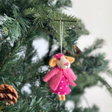 A handcrafted wool felt mouse ornament is suspended by a white string from a lush Christmas tree branch. This delightful 3D felt mouse wears a pink beaded dress, a matching jacket, and a tiny pink hat. The charming mouse ornament features light brown ears, a pink nose, and a beaded necklace, adding whimsical detail to your holiday decor.