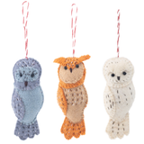 A handcrafted wool felt owl ornament, representing the Owl Family collection, is suspended by a red and white cotton string against a stark white backdrop. This unique Christmas felt ornament features simple stitched accents, small black eyes, and distinct patterns, available in varied color combinations like soft blues, grays, oranges, browns, and creamy whites.