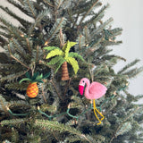A vibrant felt pineapple ornament hangs prominently on a decorated Christmas tree. This handcrafted felt ornament features a mix of yellow and orange with green leafy tops, suspended by a jute string, adding a playful, Florida-inspired touch.