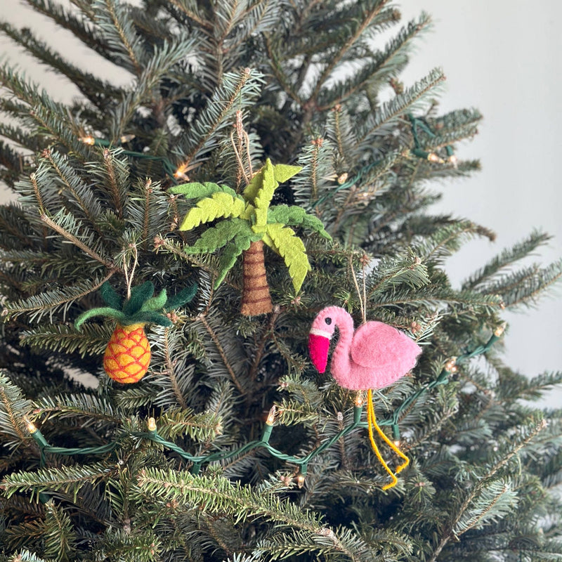A vibrant felt pineapple ornament hangs prominently on a decorated Christmas tree. This handcrafted felt ornament features a mix of yellow and orange with green leafy tops, suspended by a jute string, adding a playful, Florida-inspired touch.