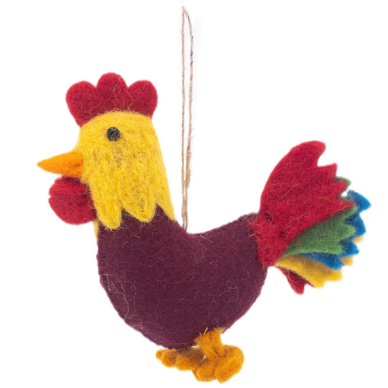 A charming handmade rooster wool felt ornament is suspended by a jute string against a crisp white background, ready for hanging. This unique Christmas ornament features a fluffy yellow head with a bright red comb and wattle, and an orange beak. Its body is rich burgundy, with tail feathers fanning out in vibrant layers of red, green, yellow, and blue. Tiny yellow wool felt feet peek from the bottom.