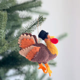 A playful wool felt koala and baby ornament hangs on a lush green Christmas tree, against a soft white backdrop. This handcrafted felt ornament depicts a light grey mother koala with a smaller baby on her back, both featuring darker grey details. A jute string is attached for hanging.