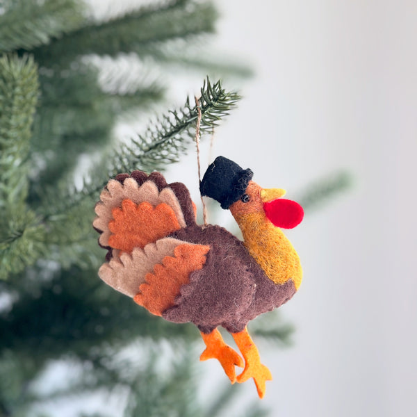 A playful wool felt koala and baby ornament hangs on a lush green Christmas tree, against a soft white backdrop. This handcrafted felt ornament depicts a light grey mother koala with a smaller baby on her back, both featuring darker grey details. A jute string is attached for hanging.