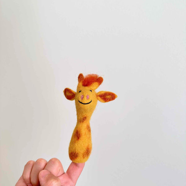 A hand holds a small, plush giraffe finger puppet made from wool felt, featuring a friendly face with a big smile, large eyes, and a patterned body resembling fur texture. The background is plain white, contrasting with the colorful puppet. This handmade needle-felted giraffe finger puppet is perfect for kids' imaginative playtime.
