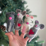A handmade felt mouse finger puppet is playfully displayed on a female hand against a blurred, festive Christmas tree backdrop. This charming felt mouse finger puppet features a pink nose and delicate whiskers, crafted from soft premium felt. Its handcrafted design makes it an ideal felt toy for kids' interactive storytelling and imaginative play, embodying fair-trade craftsmanship.