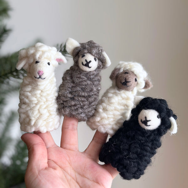 A hand holds three wool felt finger puppets, arranged in a triangular formation on fingers. The top puppet has a smiling face, while the bottom ones have neutral expressions. Each puppet is made of soft, fluffy woolly material.