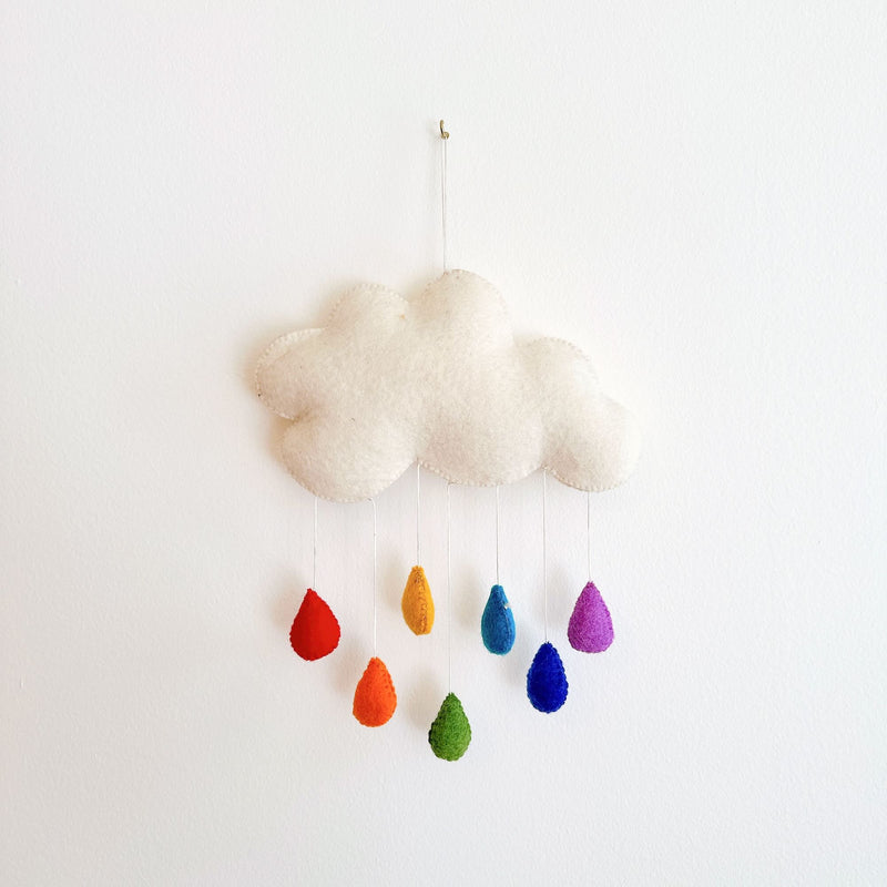 A colorful felt cloud wall decoration with raindrops in various colors of the rainbow, resting on a table or shelf, featuring a fluffy white cloud adorned with vibrant wool felt raindrops. The cloud is white, and the raindrops are attached to it, creating a playful and whimsical scene. This wool felt garland adds a cute and playful touch to any kid's room.