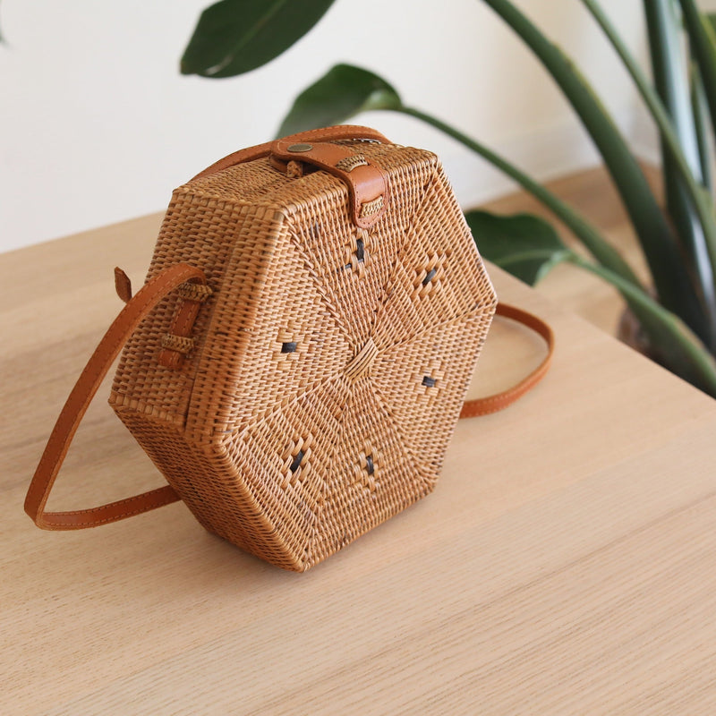 Bali Hexagon Rattan Crossbody Bag by Ganapati Crafts Co. handwoven by skilled artisans in Bali is sitting on a wood table