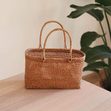 The Bali Rattan Woven Handbag handmade by Ganapati Crafts Co. in Bali is sitting a wood table looking stylish