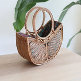 The Tulip Bali Rattan Clutch handmade by Ganapati Crafts Co. in Bali where all the Bali Rattan Bags are made is sitting on a wood table looking stylish