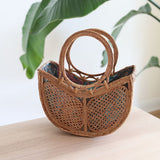 The Tulip Bali Rattan Clutch handmade by Ganapati Crafts Co. in Bali where all the Bali Rattan Bags are made is sitting on a wood table looking stylish
