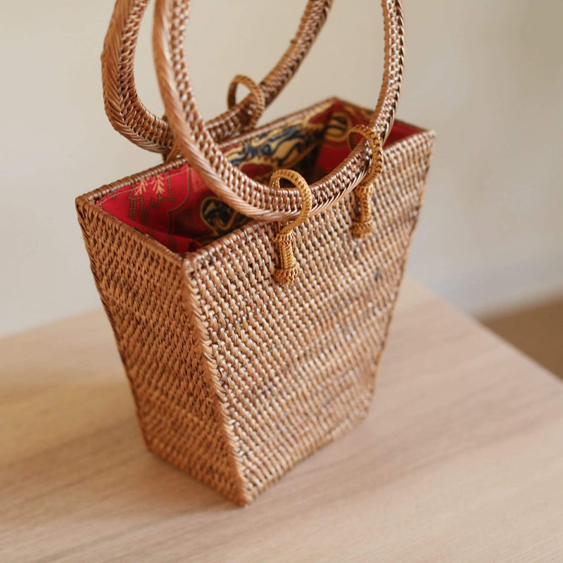 The Bali Trapezoid Rattan Handbag handmade by Ganapati Crafts Co. in Bali is sitting on a wood table