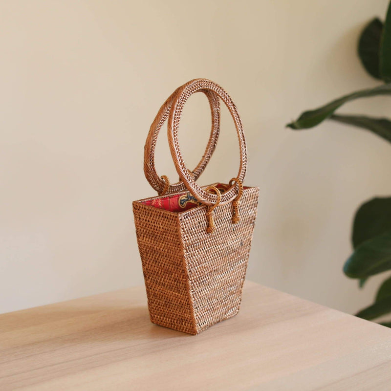 The Bali Trapezoid Rattan Handbag handmade by Ganapati Crafts Co. in Bali is sitting on a wood table